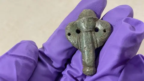 Rugby Borough Council A hand wearing a purple glove, holding a small medieval metal dagger tip