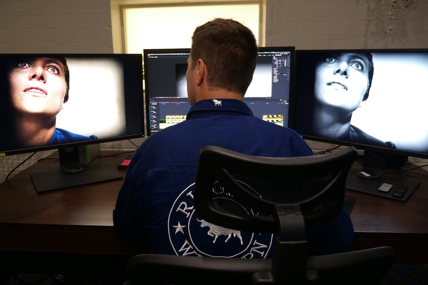 A man sits at his desk working with colourisation software. 