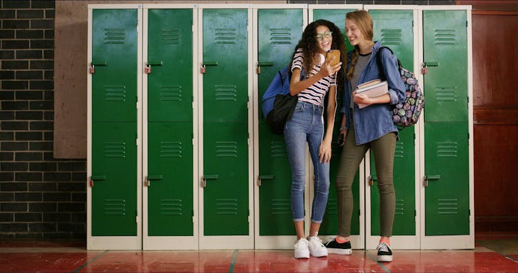 Two girls in a school laughing at a phone