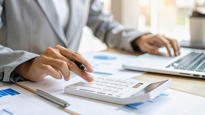 A person sitting at a table doing finances on a computer and calculator