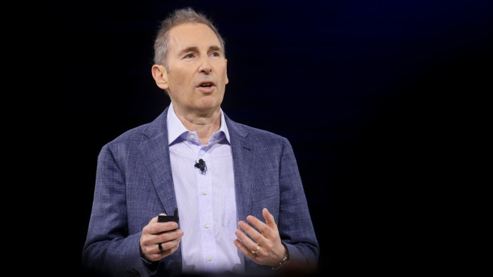 Andy Jassy speaks on stage, gesturing with one hand and holding a device, during Amazon’s Alexa AI overhaul event.