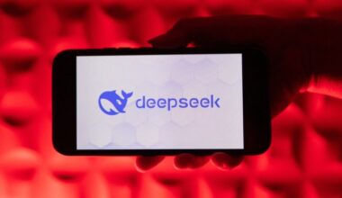 A hand holds a smartphone displaying the Deepseek AI logo against a vivid red illuminated background.