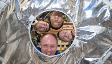Four people look through a circular hole in a silver metallic fabric. Clockwise from left are JAXA (Japan Aerospace Exploration Agency) astronaut Kimiya Yui and NASA astronauts Jonny Kim, Zena Cardman, and Mike Fincke.