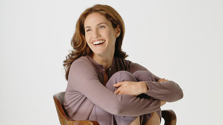 Amy Brenneman as Amy sitting on chair, smiling and squeezing her legs in Judging Amy