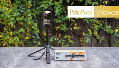 A smartphone mounted on a compact, extended tripod stands on a concrete surface outdoors. Next to it is the tripod's packaging box. In the background, leafy greenery and a "PetaPixel Showcase" banner are visible.