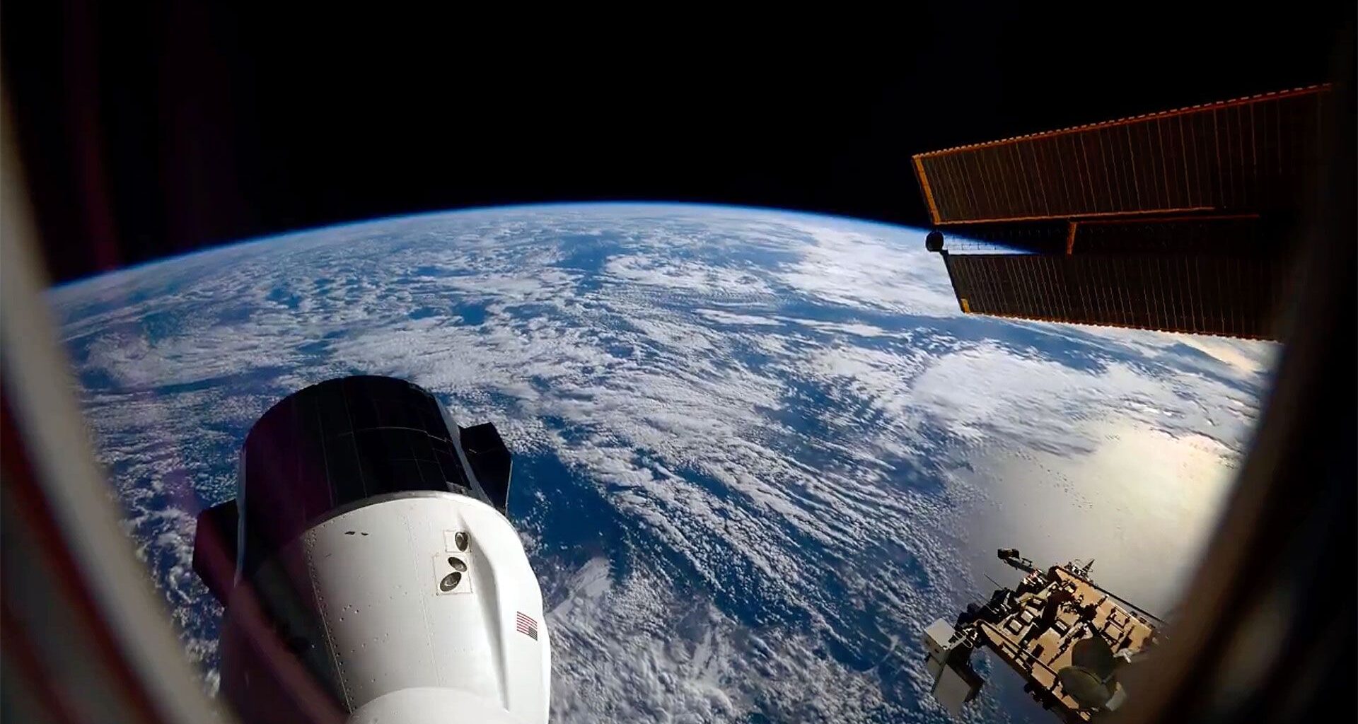 the blue waters and white clouds stretch to out to Earth's horizon, set against the blackness of space; in the foreground, a space capsule extends out from a space station