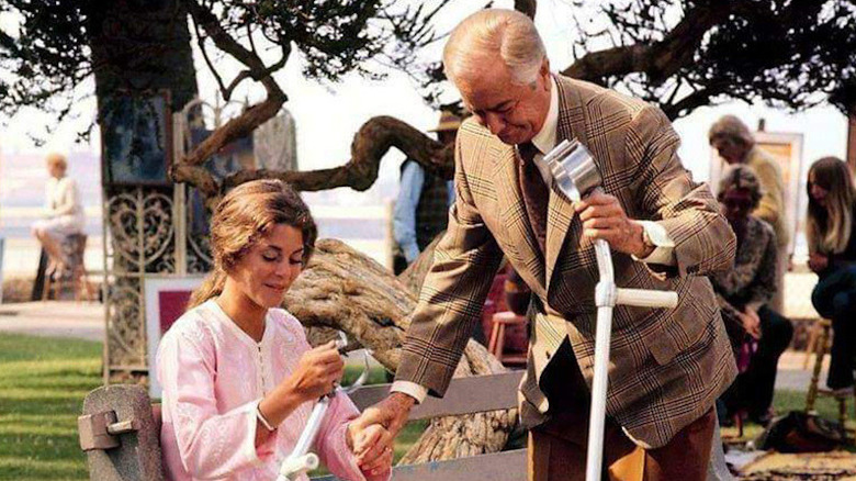 Lindsay Wagner as Denise wearing pink and sitting on bench with crutch next to Robert Young as Dr. Welby in suit, also holding crutch, in Marcus Welby, M.D.