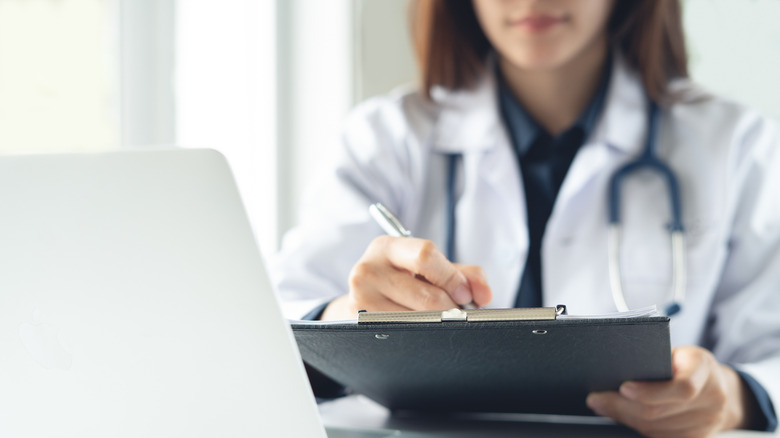 A doctor with a clipboard sitting behind a laptop