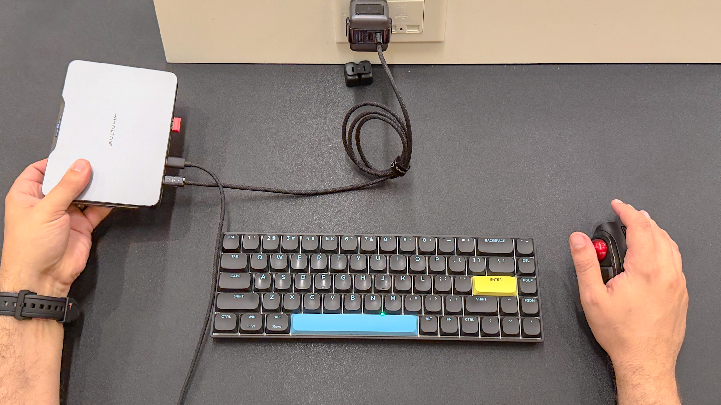 The Khadas Mind 2S mini PC in hand with a wireless mechanical keyboard and a trackball mouse