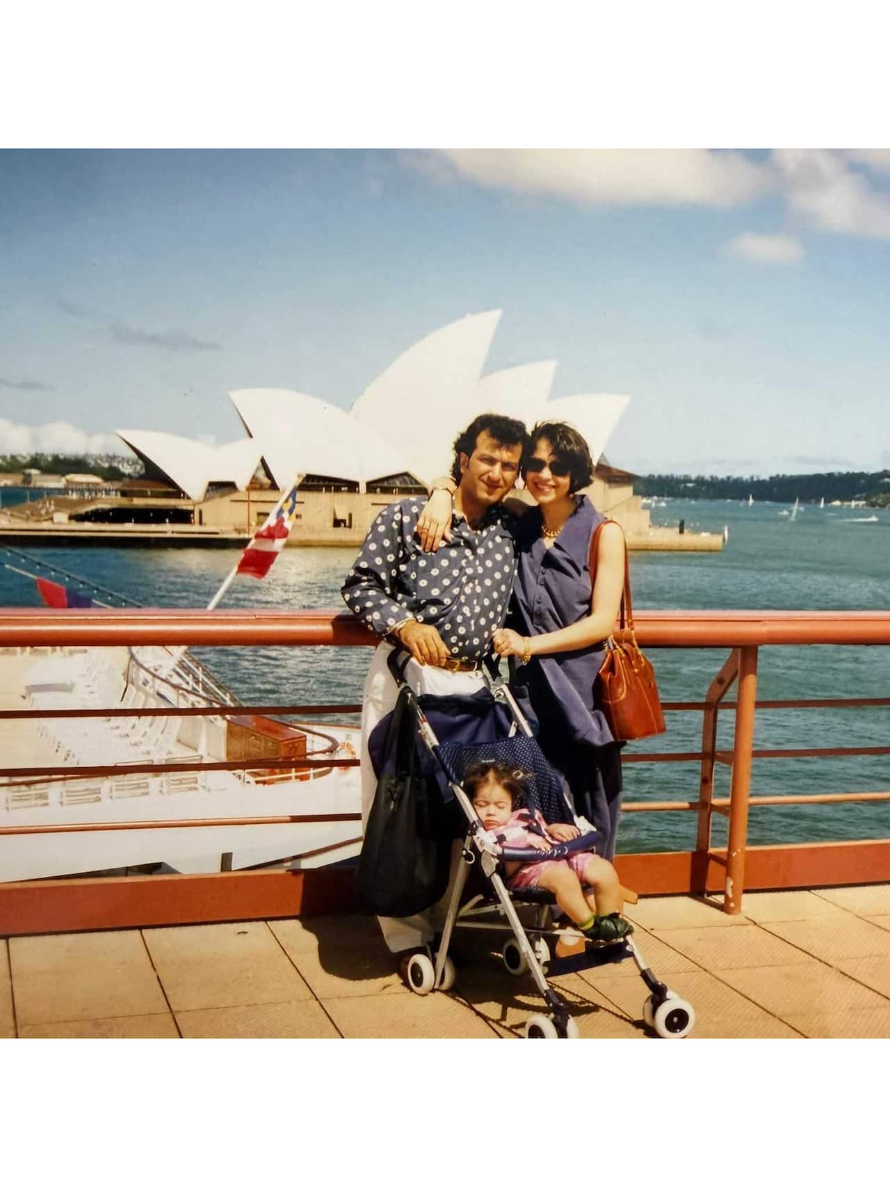 Two parents and a child in a stroller in front of the Sydney Opera House