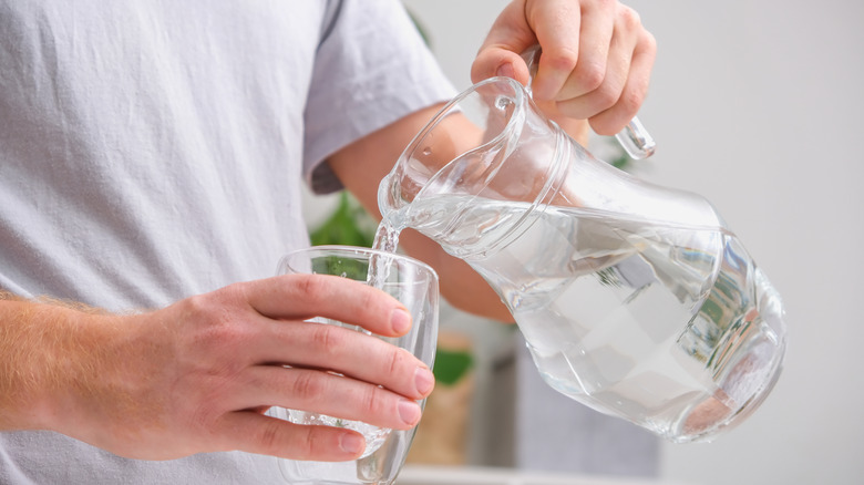 Hands pouring water into glass from pitcher