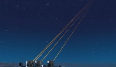 A series of small round buildings at the bottom left of the image with four yellow lasers pointing into the top right of the image over a dark blue night sky.