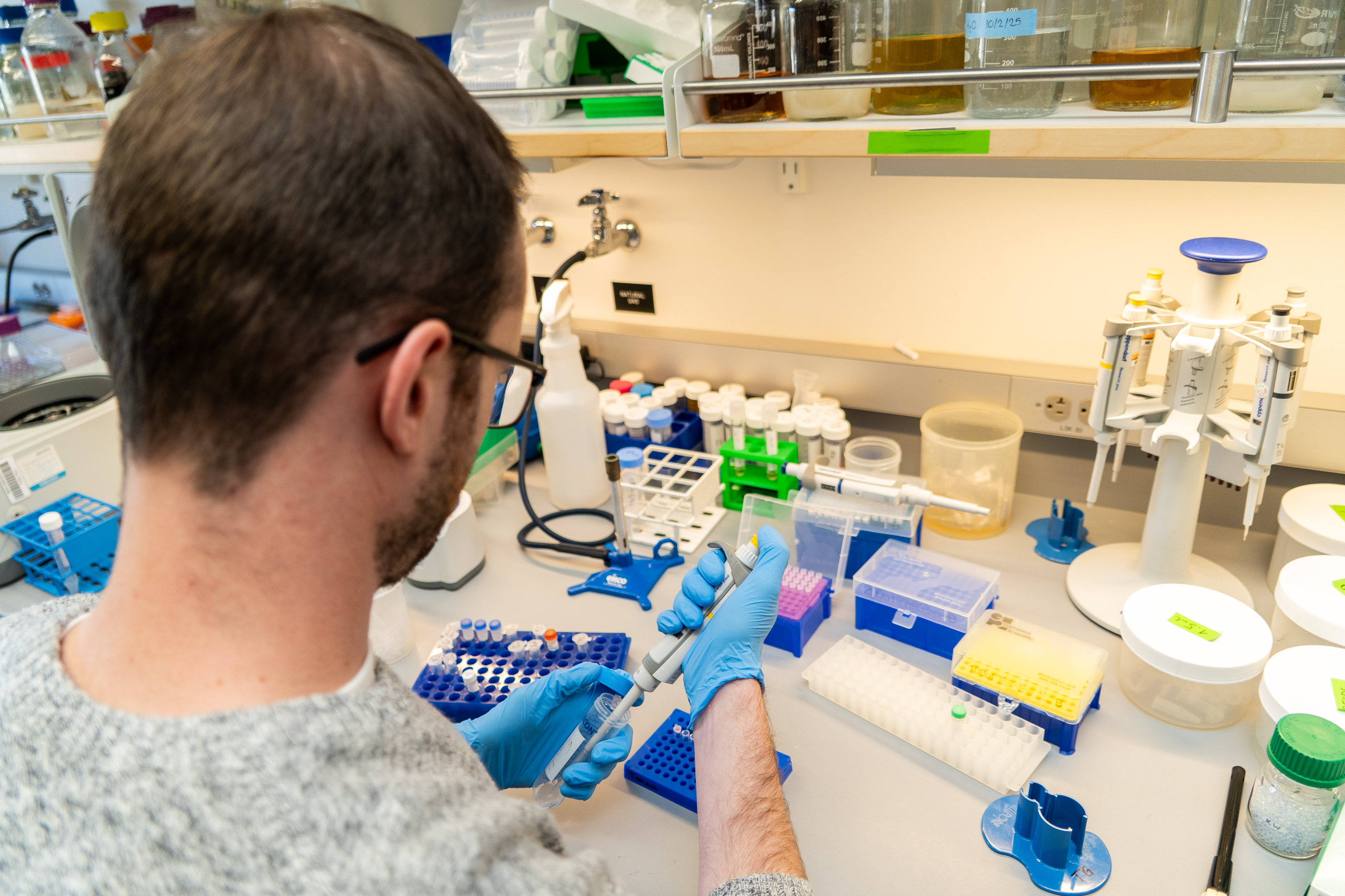 Noah Robinson pipetting in a lab to write genetic codes for synthetic life.