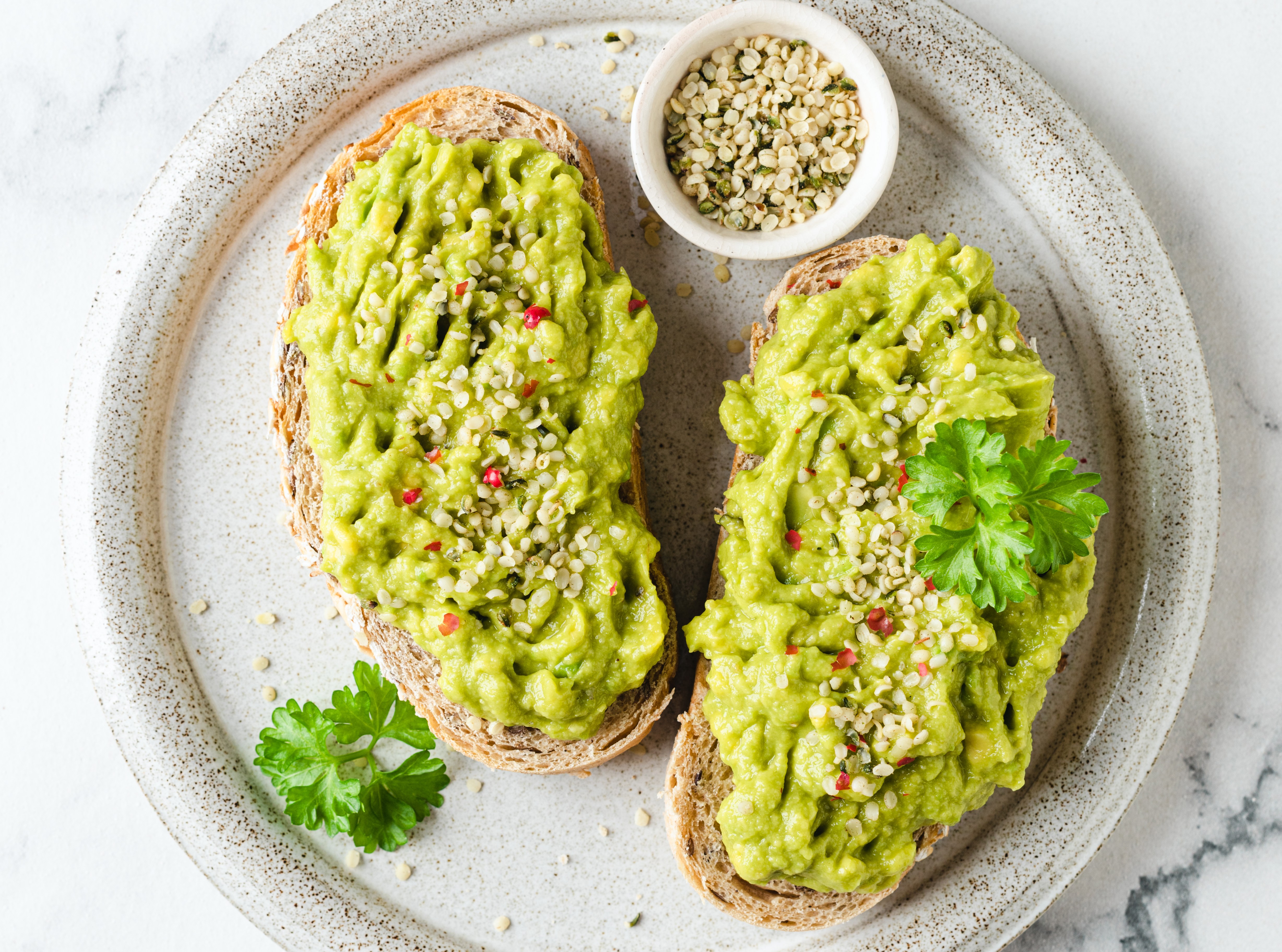 Two pieces of avocado toast with hemp seeds on a speckled plate.