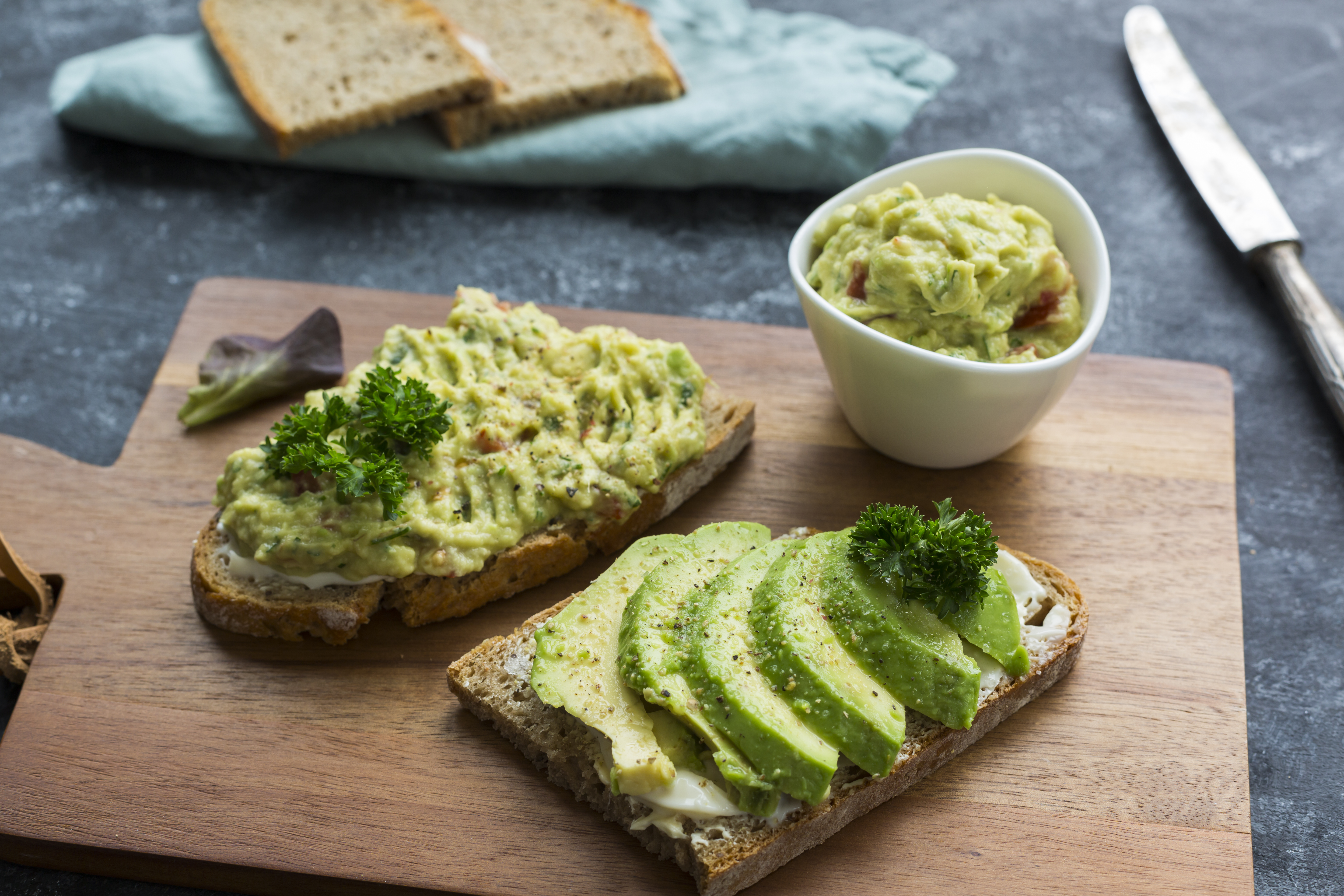 Avocado cream and sliced avocado on bread on a wooden board.