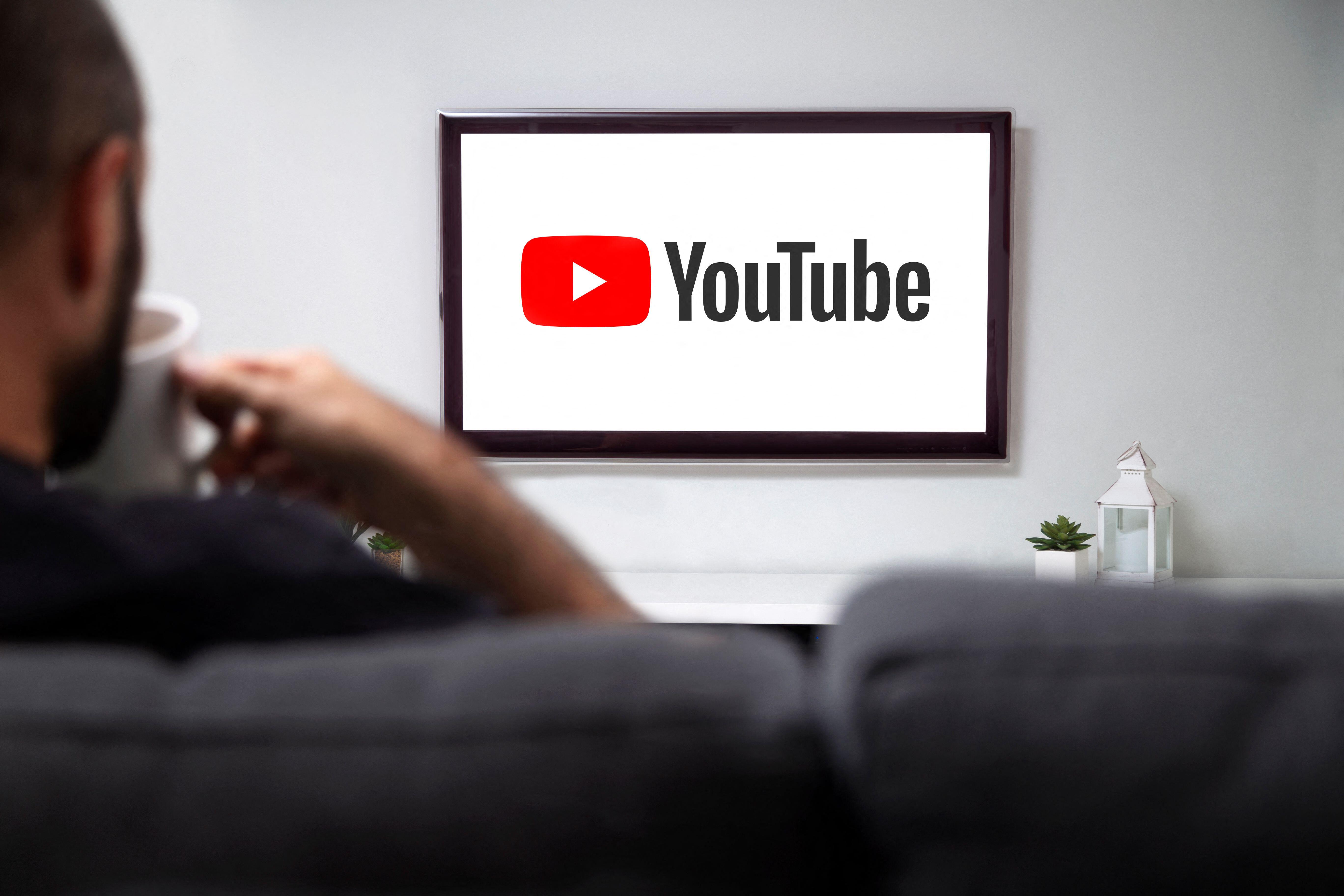 Man watching a YouTube logo on a smart TV while holding a mug.