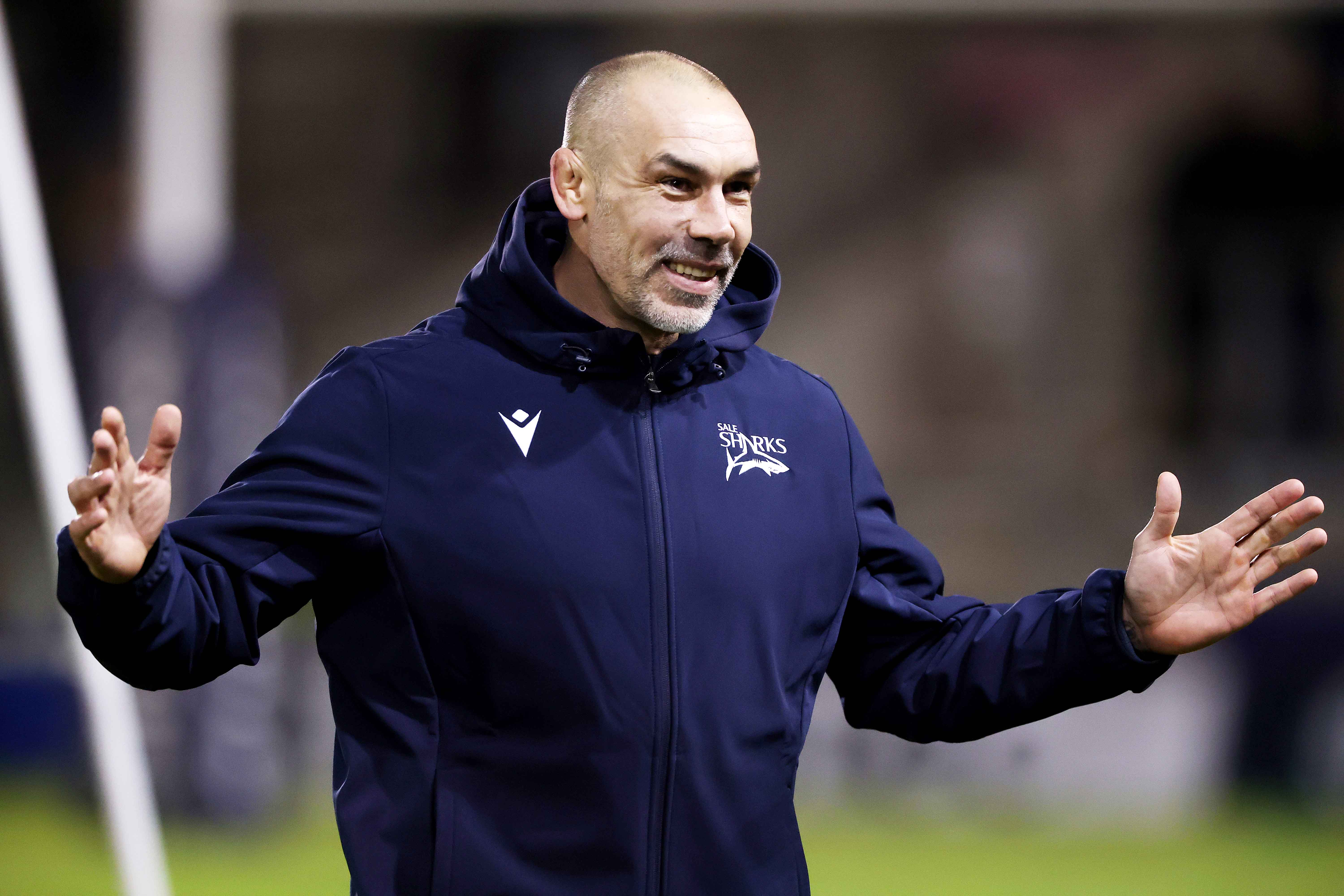 Alex Sanderson, director of rugby for Sale Sharks, smiles while wearing a navy blue jacket with the team's logo.