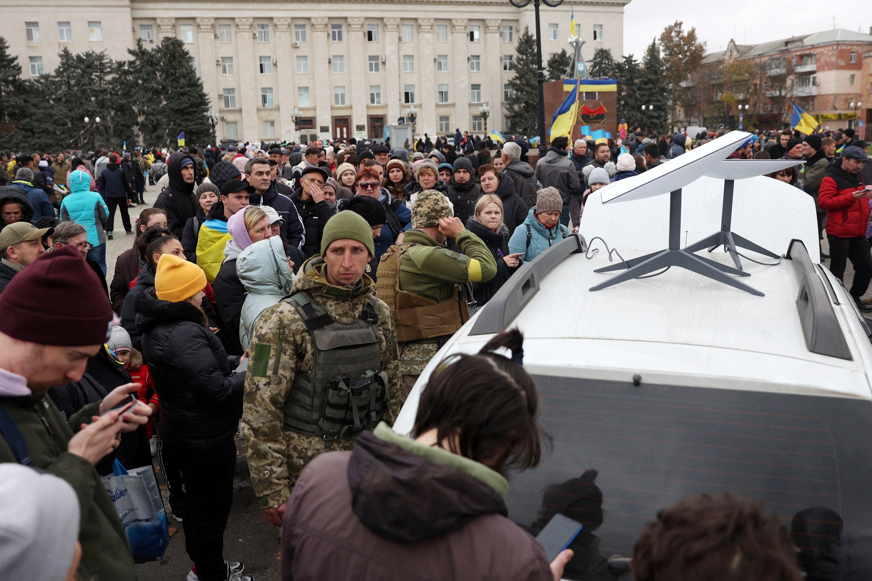 Ukrainians using mobile phones near a Starlink satellite dish on a car in Kherson.