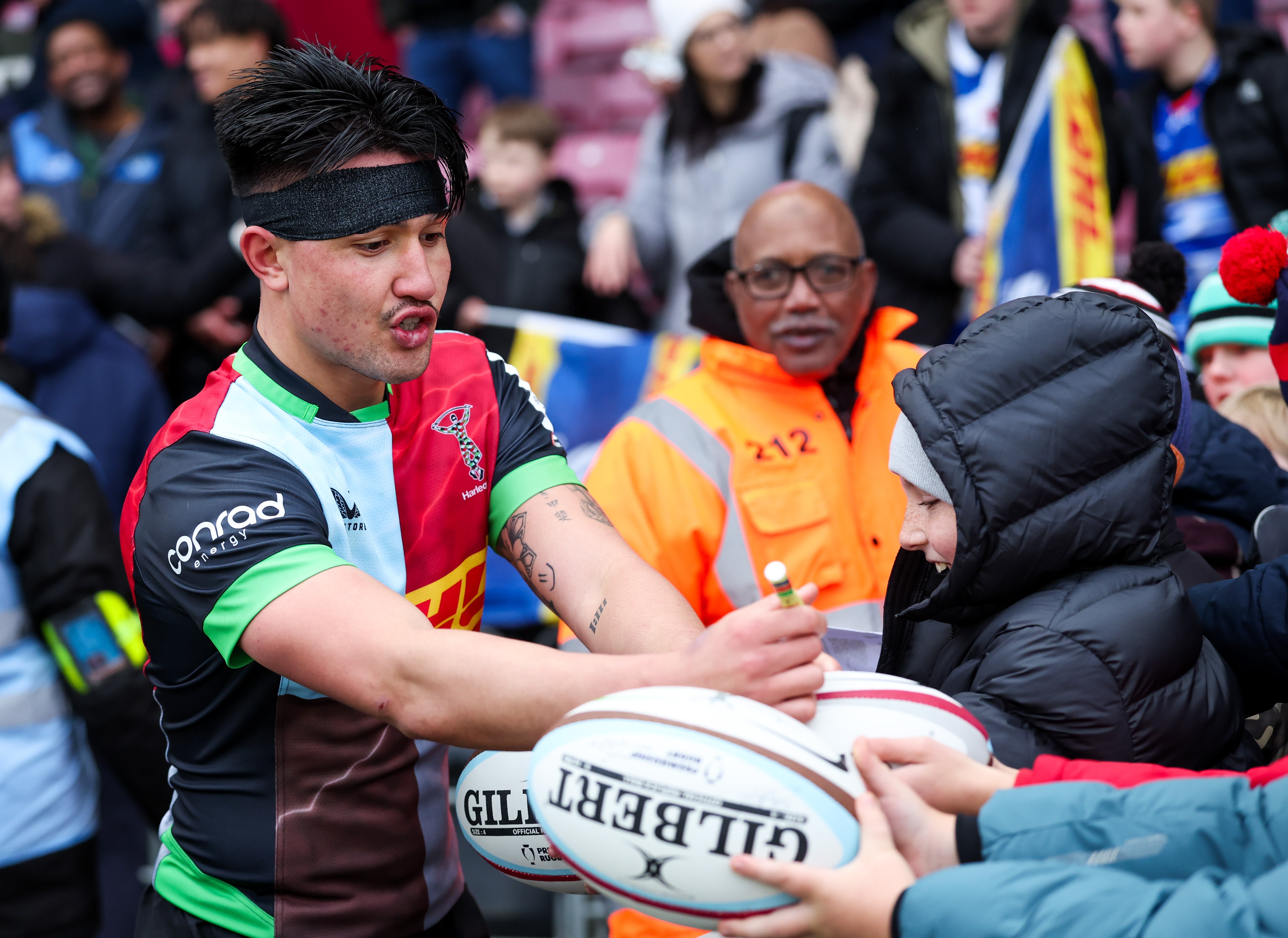 Marcus Smith of Harlequins signing an autograph on a rugby ball for a young fan.