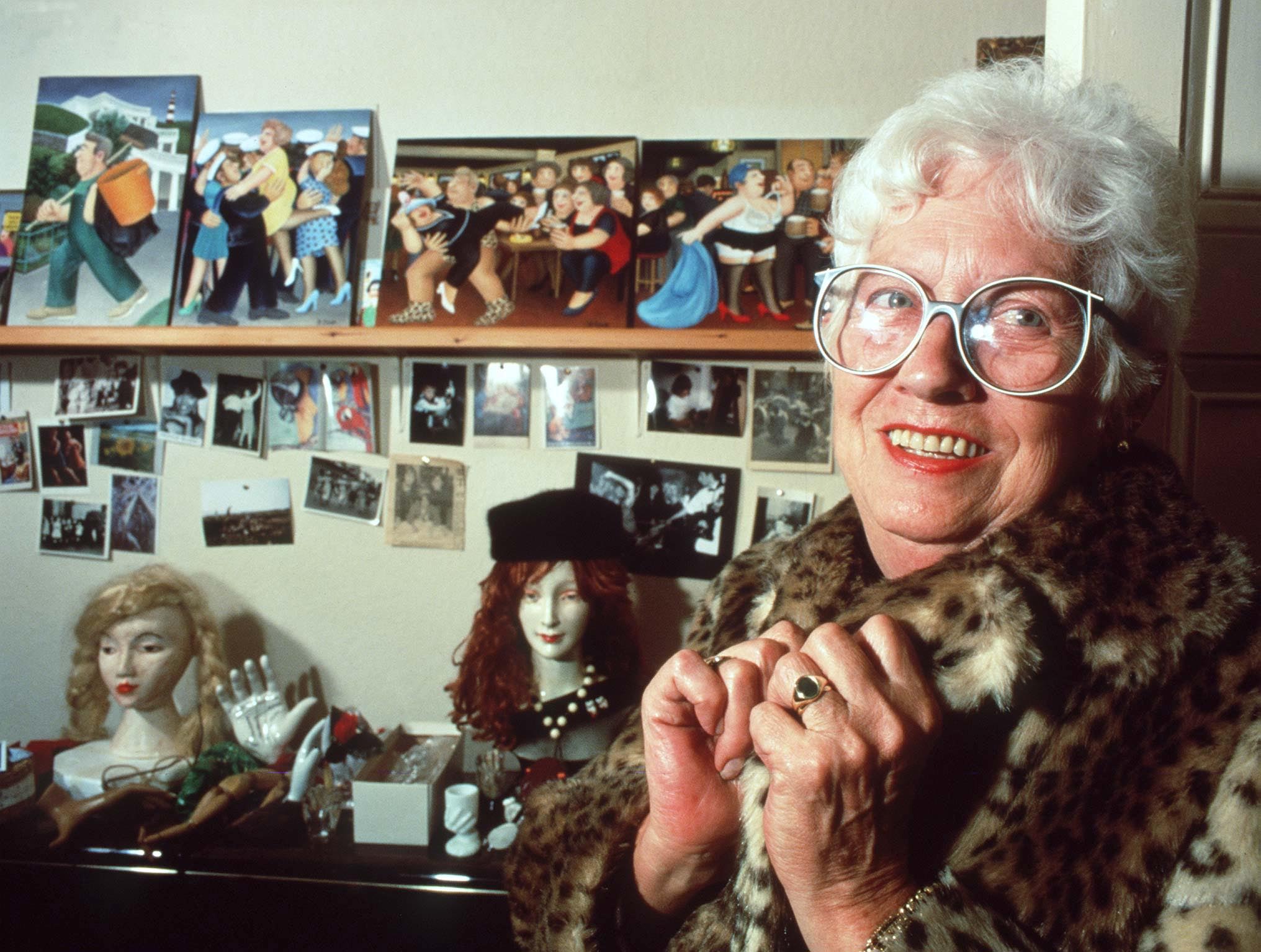 Artist Beryl Cook, known for her humorous paintings of plump women, stands in a leopard print coat in front of her artwork.
