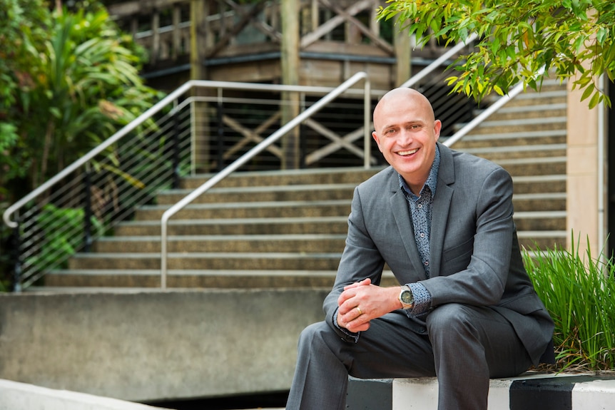a man wearing a suit sits on stairs and smiles