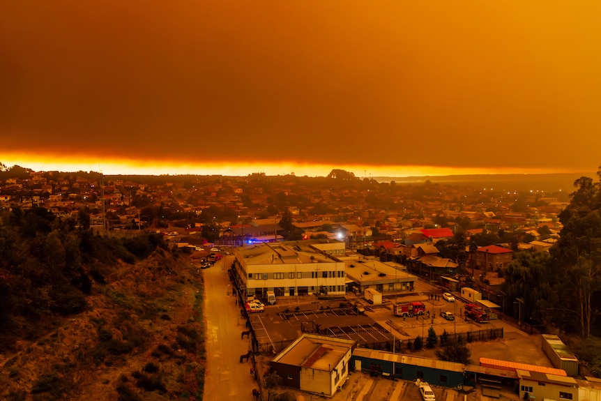 Wildfires seen burning at sunrise over a city. Everything is in an orange hue.