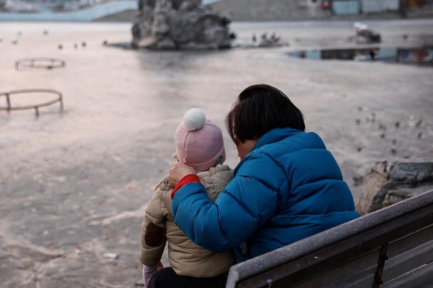 An older Asian woman and a child at an icy park in winter.