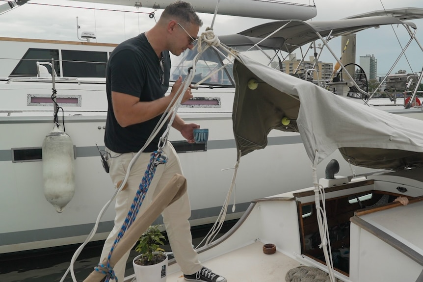A man in a dark t shirt standing on a yacht deck