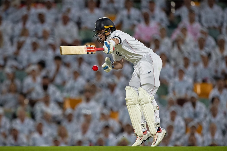 A cricketer in white is struck by a pink ball while holding his bat