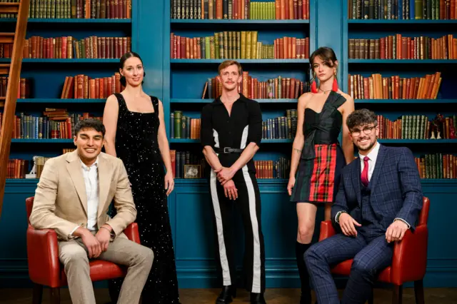 The five people who were left in the final stand and sit. Faraaz and Jack sit, while Stephen, Jade and Rachel stand. They smile in front of large bookcases.