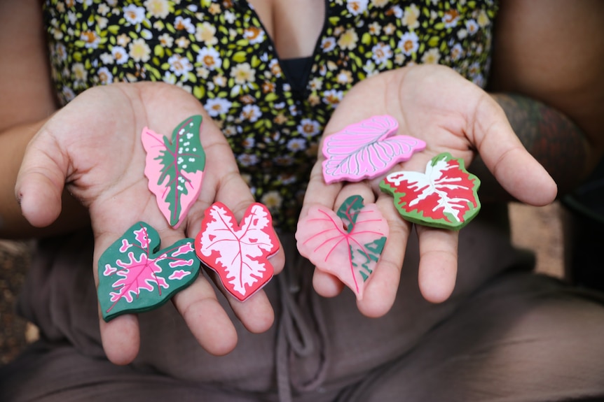 A woman holding magnets shaped like caladiums.