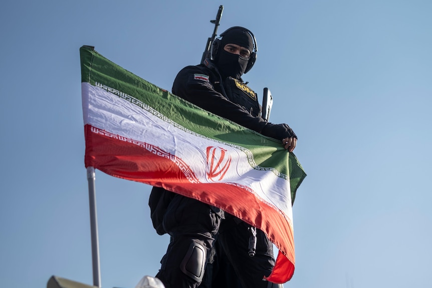 An armed member of Iran's police special forces adjusts a flag.