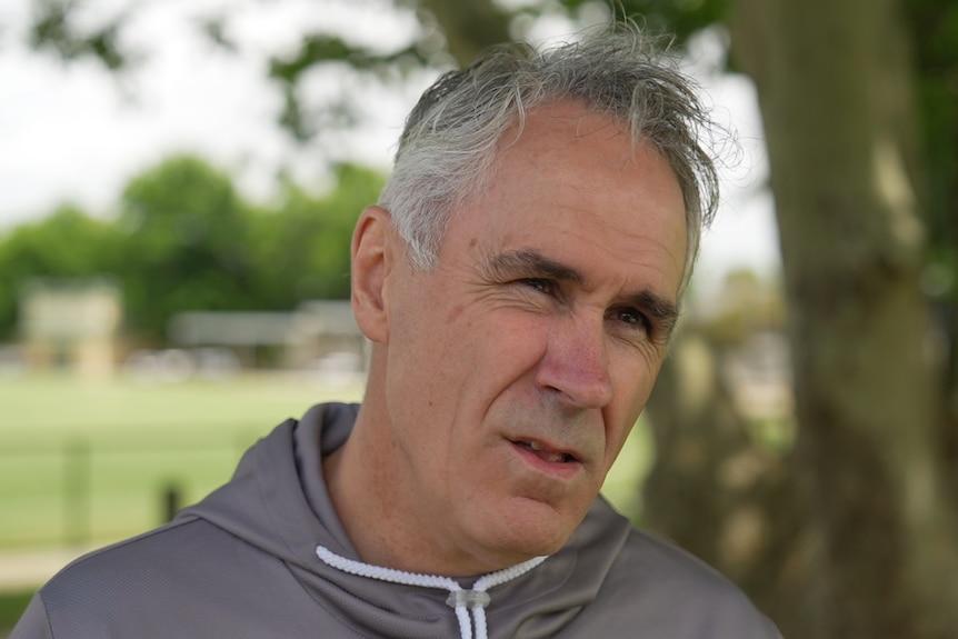 A man standing outdoors near a cricket field.