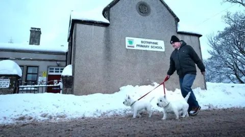 Getty Images A member of the public with two small white dogs passes Botriphine Primary amid snow.