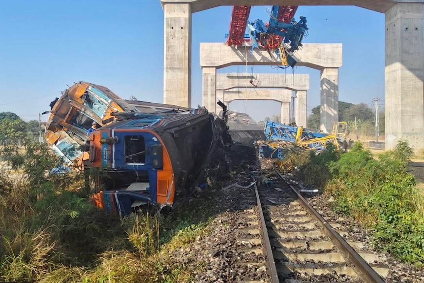 A train carriage has derailed and is heavily damaged and lying on its side. 
