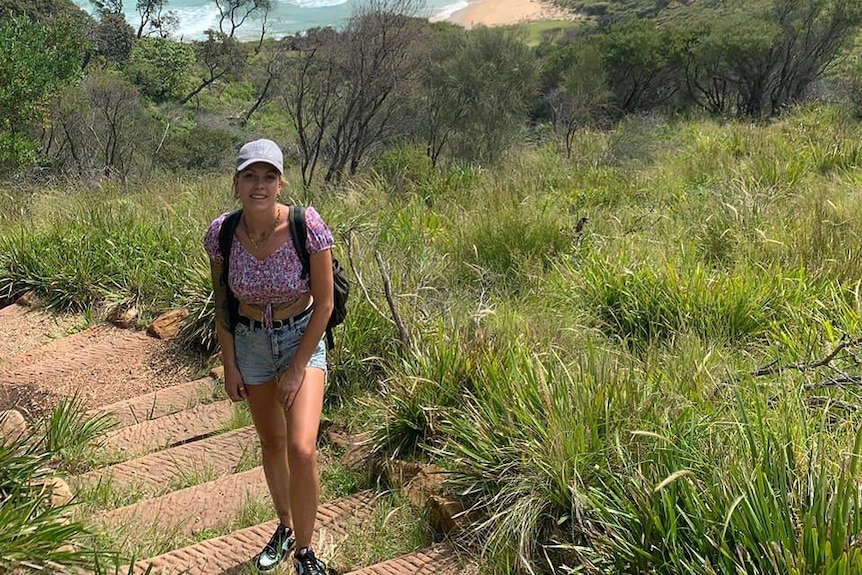 A young woman poses for a photo on a walking track near coastal area.