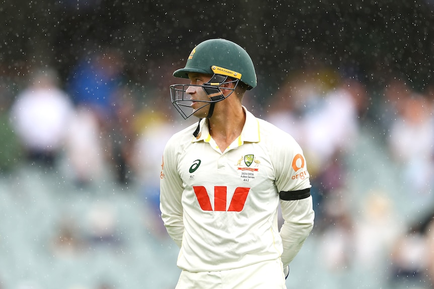 Australia wicketkeeper Alex Carey stands on the field as rain falls during a cricket Test.