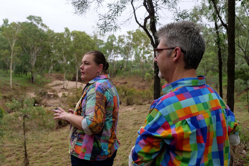 A man and a woman are outside looking at a creek bed.