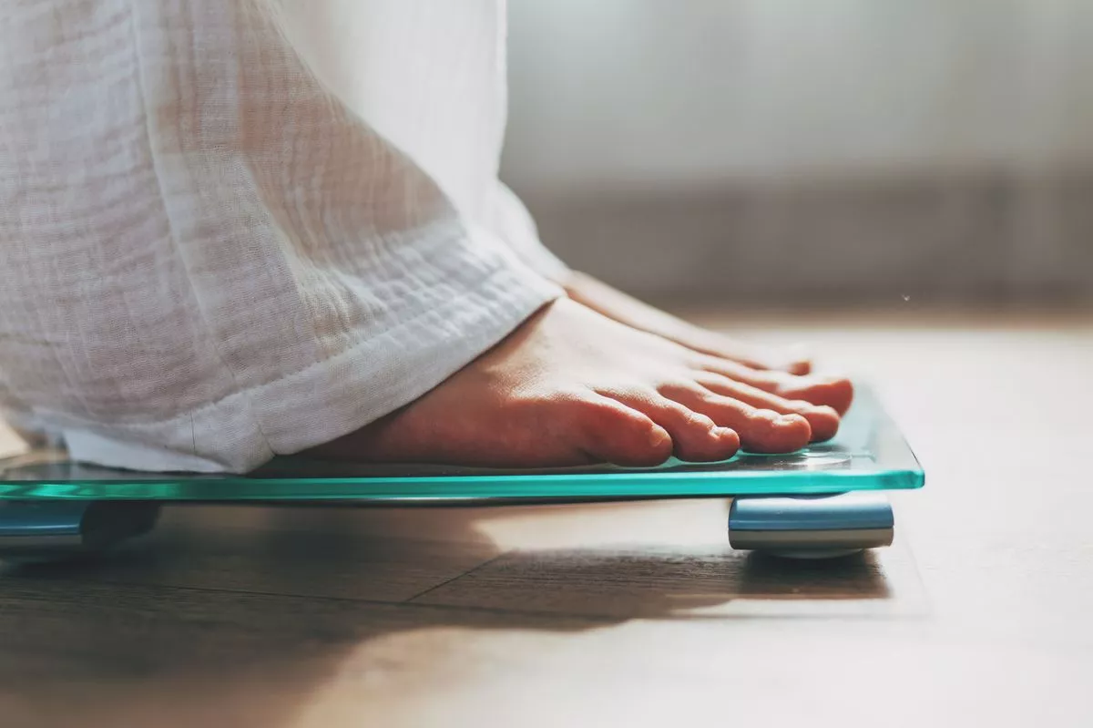 Female feet standing on electronic scales for weight control on wooden background. The concept of slimming and weight loss