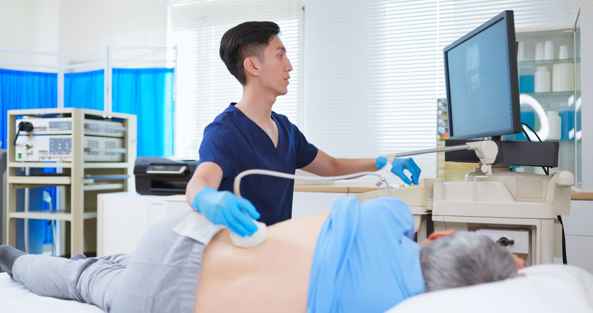 asian old man is in clinic lying side on treatment bed - the young male doctor use kidney ultrasound to check his health