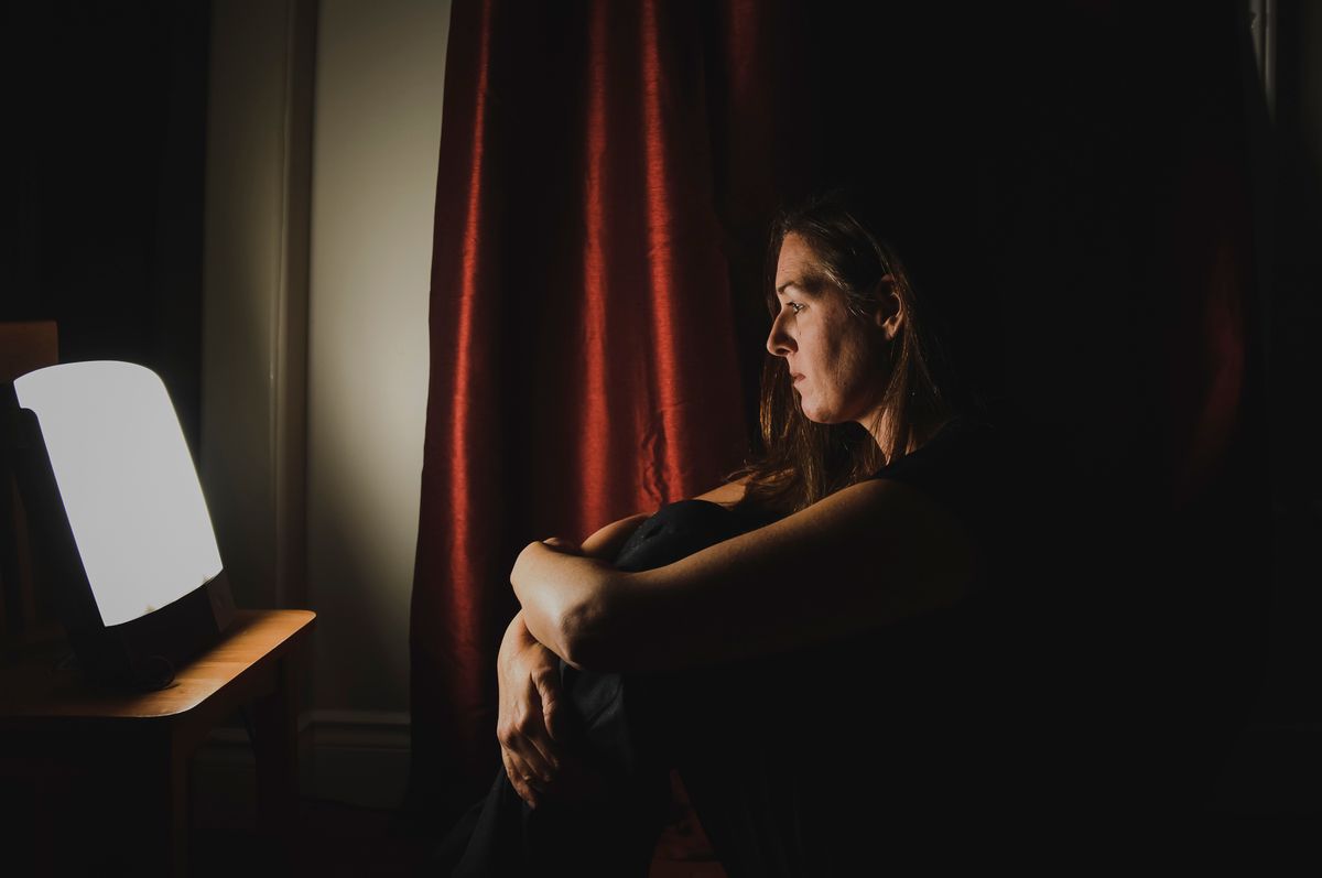 Profile of woman sitting looking at light therapy lamp in a dark room