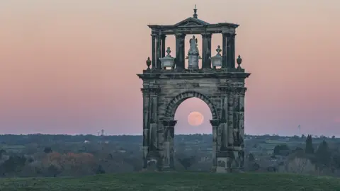 Ian Knight / Z70 Photography The moon is visible through the arch of a monument standing on a field