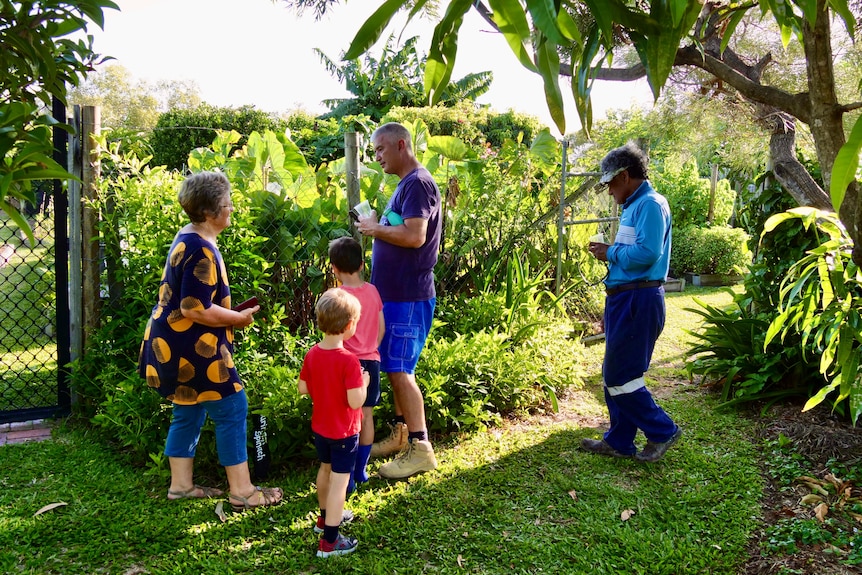 A group of five people walking around a green garden talking.