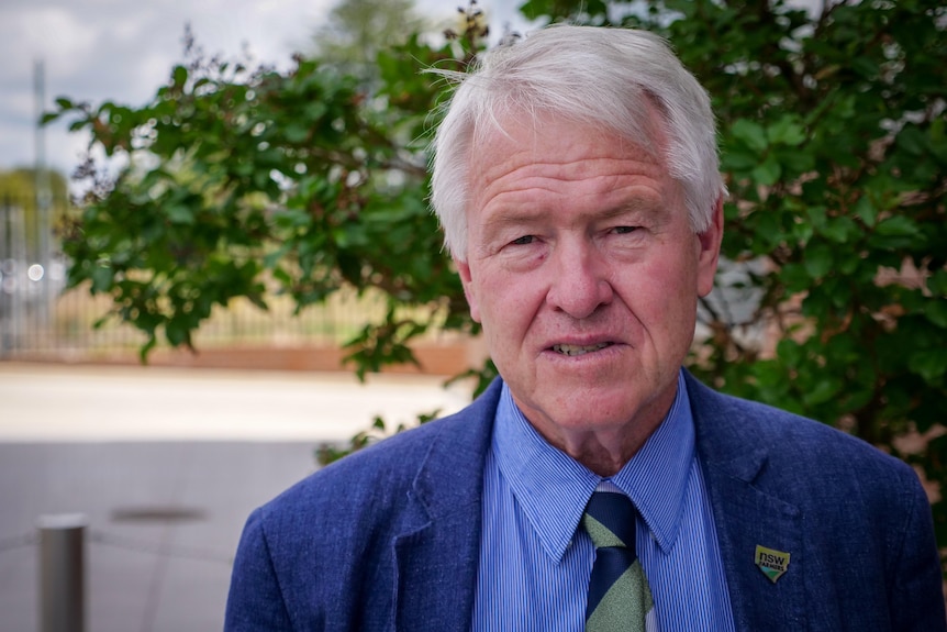 Mid close up of a man in a tie and suit jacket looks to camera.