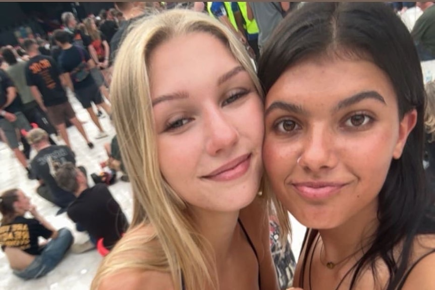 Two young women with their heads together with at a concert.