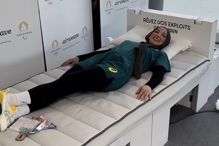 Australian Tina Rahimi lays on a cardboard bed smiling.