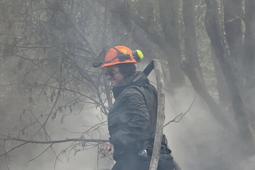 A young woman wearing an orange helmet with a hose over her shoulder in the bush.