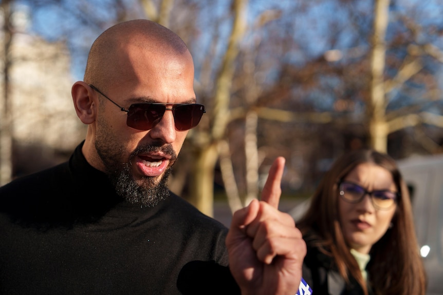A bold man in black top gestures while he is speaking