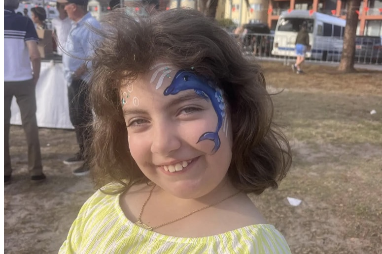 Matilda is smiling, she has a dolphin painted on her face.