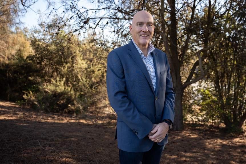 Michael Bailey, wearing a suit, standing in front of bushland.